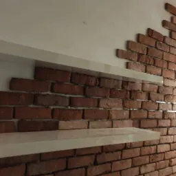 Fragment ściany z dekoracyjnej cegły z półkami w jasnym kolorze, obok widoczny regał na wino i fragment wyposażenia kuchni.