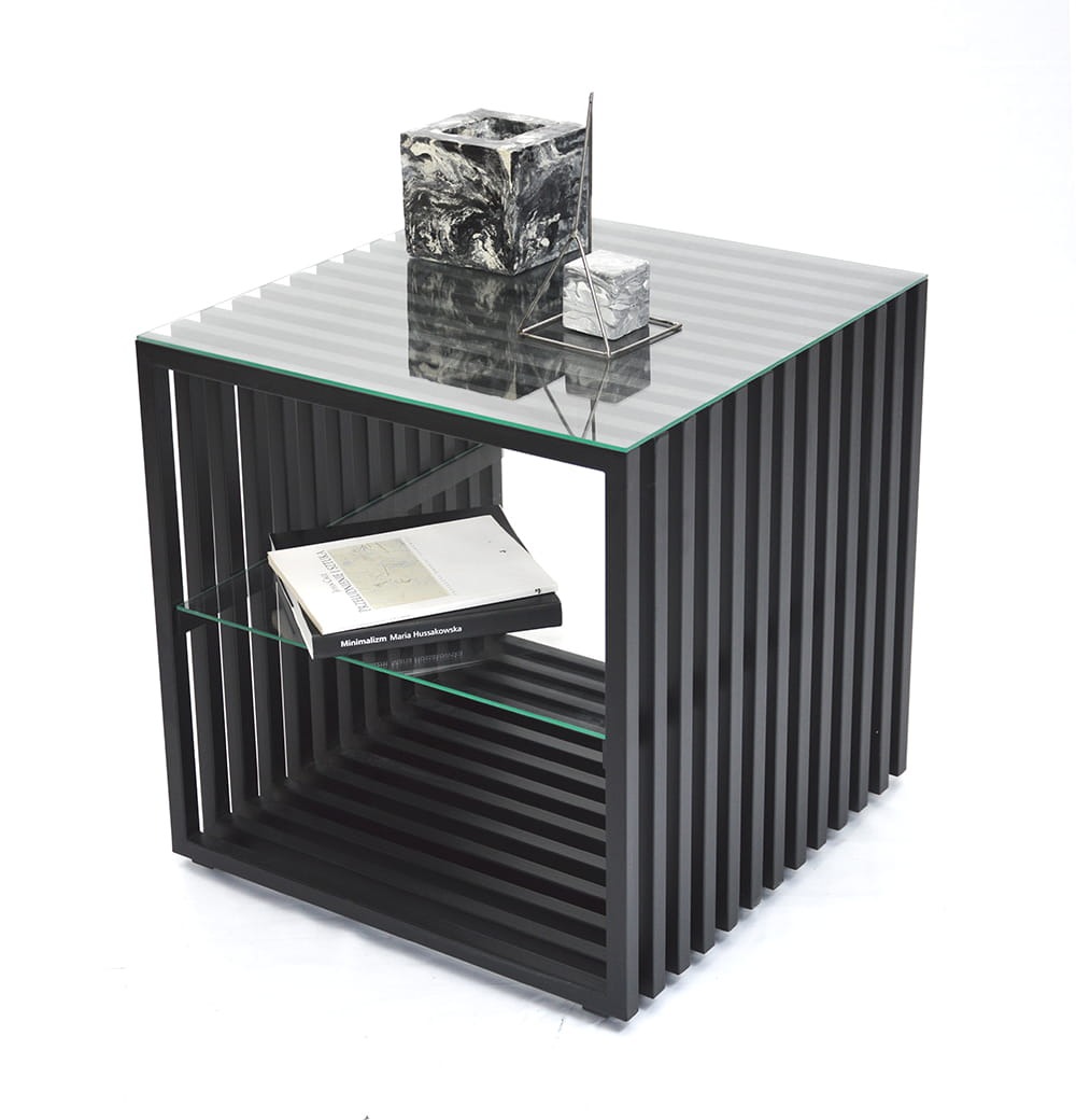 Czarny stolik kawowy o geometrycznej konstrukcji z listew, szklanym blatem i półką, na której leży książka 'Minimalizm Maria Hussakowska', na blacie dekoracyjny marmurkowy sześcian i metalowa ozdoba