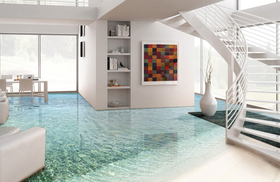 Nowoczesne wnętrze z podłogą imitującą piaszczystą plażę i płytką wodę morską, białe meble i spiralne schody, kolorowa grafika na ścianie.