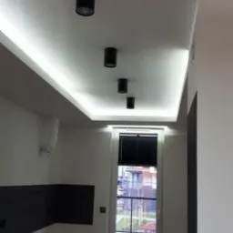 Cztery czarne reflektory sufitowe w rzędzie, podświetlony sufit LED w nowym, pustym pokoju z oknem balkonowym.