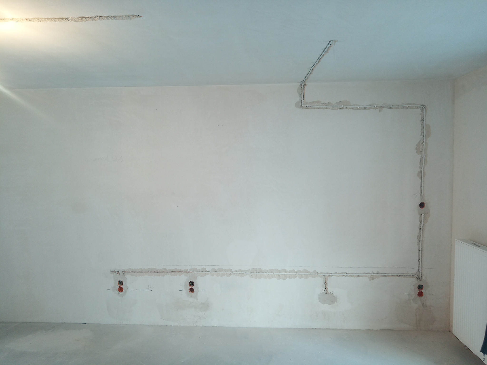 Ściana w surowym stanie z poprowadzonymi przewodami elektrycznymi w bruzdach, widoczne otwory pod gniazdka elektryczne, przygotowane do dalszych prac wykończeniowych.