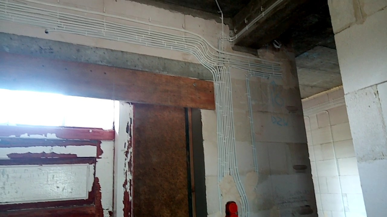 Białe rurki instalacji elektrycznej układane równolegle na surowych ścianach w trakcie remontu budynku.