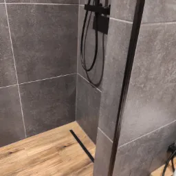 Szare, matowe płytki w kabinie prysznicowej z drewnopodobną podłogą i czarnym odpływem liniowym.