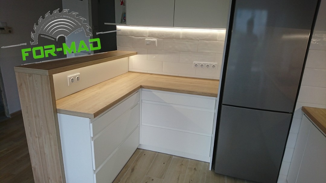 Nowoczesna zabudowa kuchenna w Lublinie z białymi frontami i drewnianym blatem, oświetlenie LED pod szafkami, widoczny fragment lodówki.