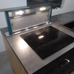 Nowoczesna kuchnia z szarą kamienną płytą, czarną płytą indukcyjną i wysuwanym okapem z oświetleniem LED, czarny zlew z baterią.