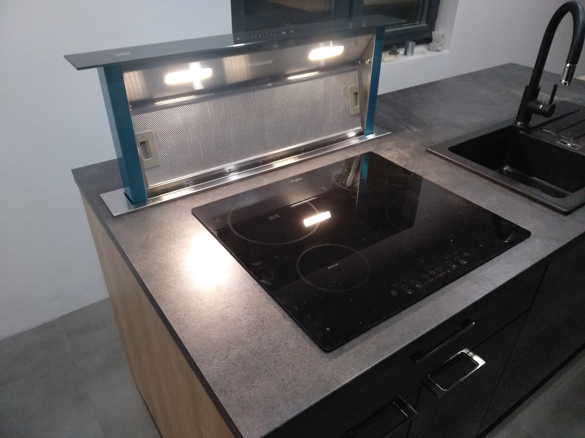 Nowoczesna kuchnia z szarą kamienną płytą, czarną płytą indukcyjną i wysuwanym okapem z oświetleniem LED, czarny zlew z baterią.