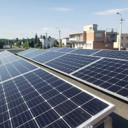 Instalacja paneli słonecznych na płaskim dachu budynku mieszkalnego, widok z góry na panele z widocznymi elementami montażowymi, w tle zabudowa miejska i błękitne niebo.