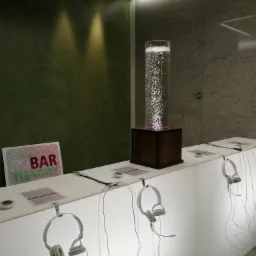 Bar tlenowy z białym, podświetlonym blatem, na którym wiszą słuchawki. W tle zielona ściana z motywem liści i kolumna z bąbelkami powietrza.