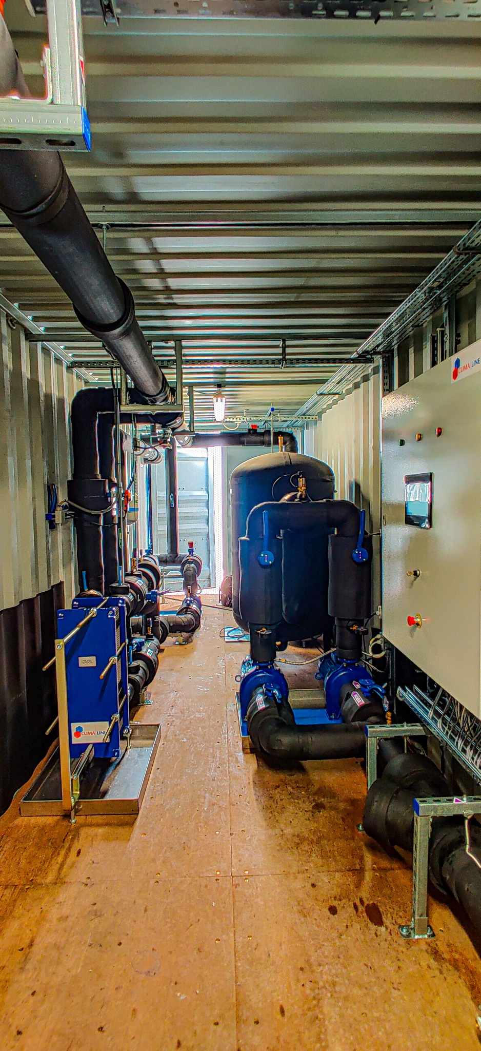 Wnętrze kontenera z zamontowaną instalacją chłodniczą: zbiornik ciśnieniowy, pompy obiegowe, orurowanie z izolacją termiczną, szafa sterownicza z wyświetlaczem i przyciskami, oświetlenie LED.