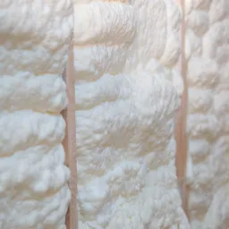 Świeżo nałożona, gęsta, biała izolacja z pianki na drewnianej konstrukcji szkieletowej, widoczne nierówności i struktura piany.