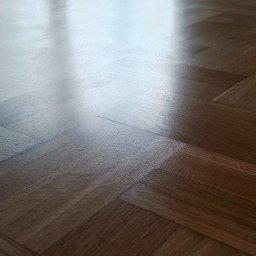 Stolarnia Białołęka Adam Cieslik - Błyszcząca, świeżo wycyklinowana drewniana podłoga ułożona w jodełkę, odbijająca światło okna z widokiem na zieleń.