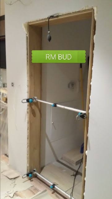 Przygotowanie ościeżnicy do montażu drzwi z użyciem rozpórki teleskopowej, widoczne niedoskonałości ściany i podłogi.