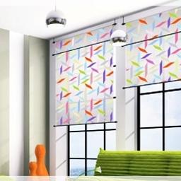 Roltex - Nowoczesne okno z dwoma panelami materiału w geometryczne wzory, zawieszonymi na czarnych rurkach, w jasnym wnętrzu z zielonymi poduszkami.
