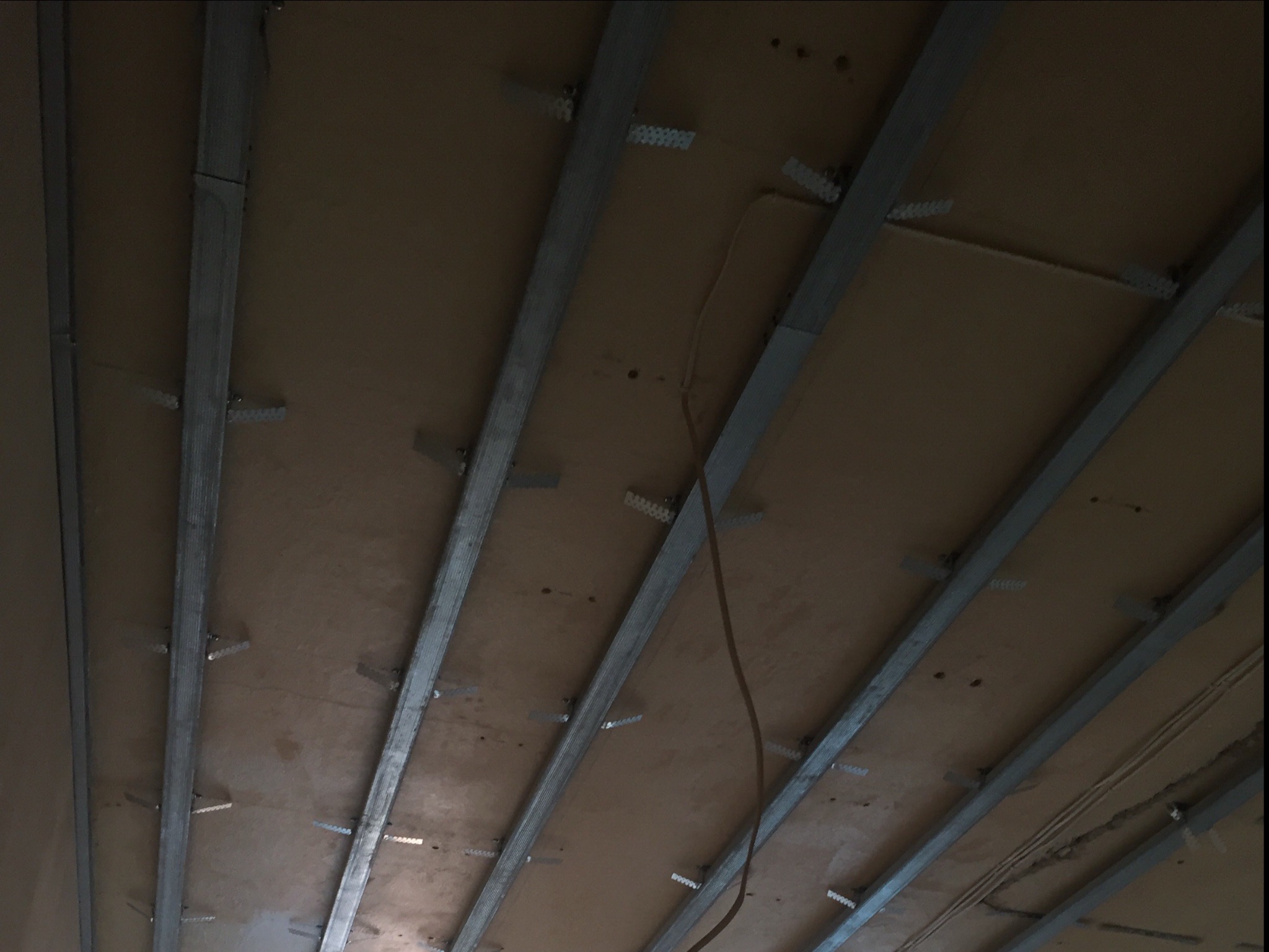 Metalowy stelaż sufitowy z płyt kartonowo-gipsowych, widok z dołu, z widocznymi elementami mocującymi i fragmentem kabla elektrycznego.