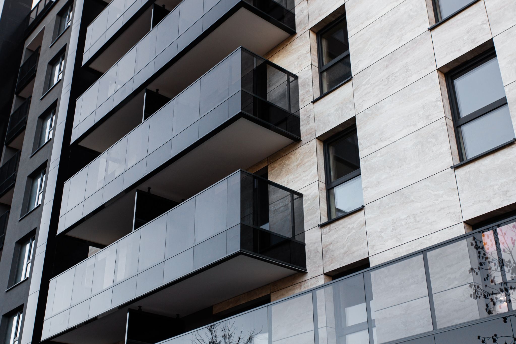 Nowoczesny budynek z balkonami z aluminiowymi ramami i szklanymi balustradami, widok z dołu na elewację z jasnego kamienia.