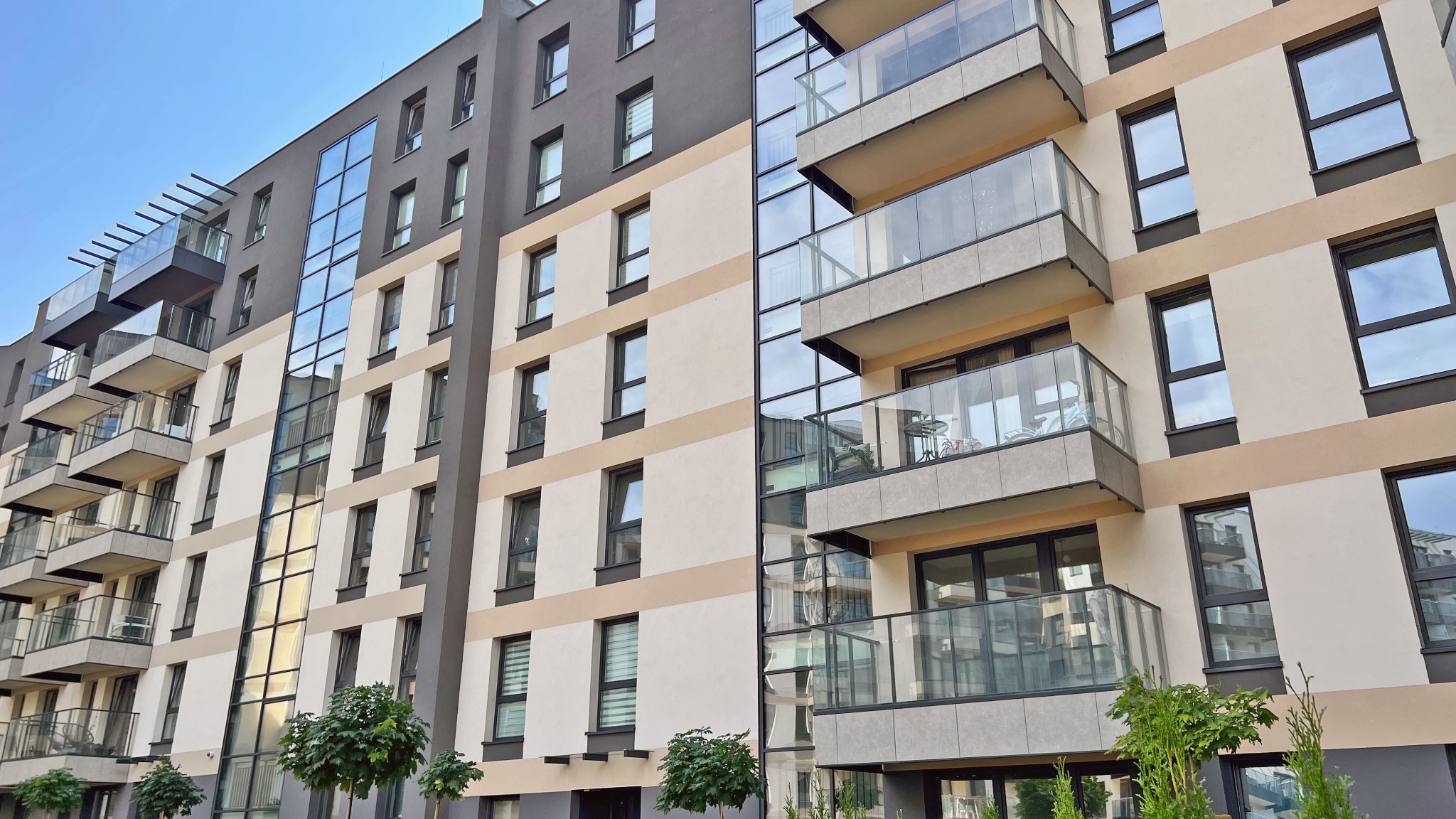 Elewacja nowoczesnego apartamentowca z oknami aluminiowymi i balkonami ze szklanymi balustradami.