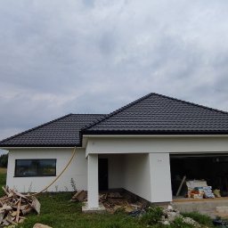 PACZO-SERVICE PAWEŁ PASZKOWSKI - Nowo wybudowany dom jednorodzinny z ciemną dachówką i białymi ścianami, widoczny z boku, z elementami w trakcie wykończenia wokół budynku.