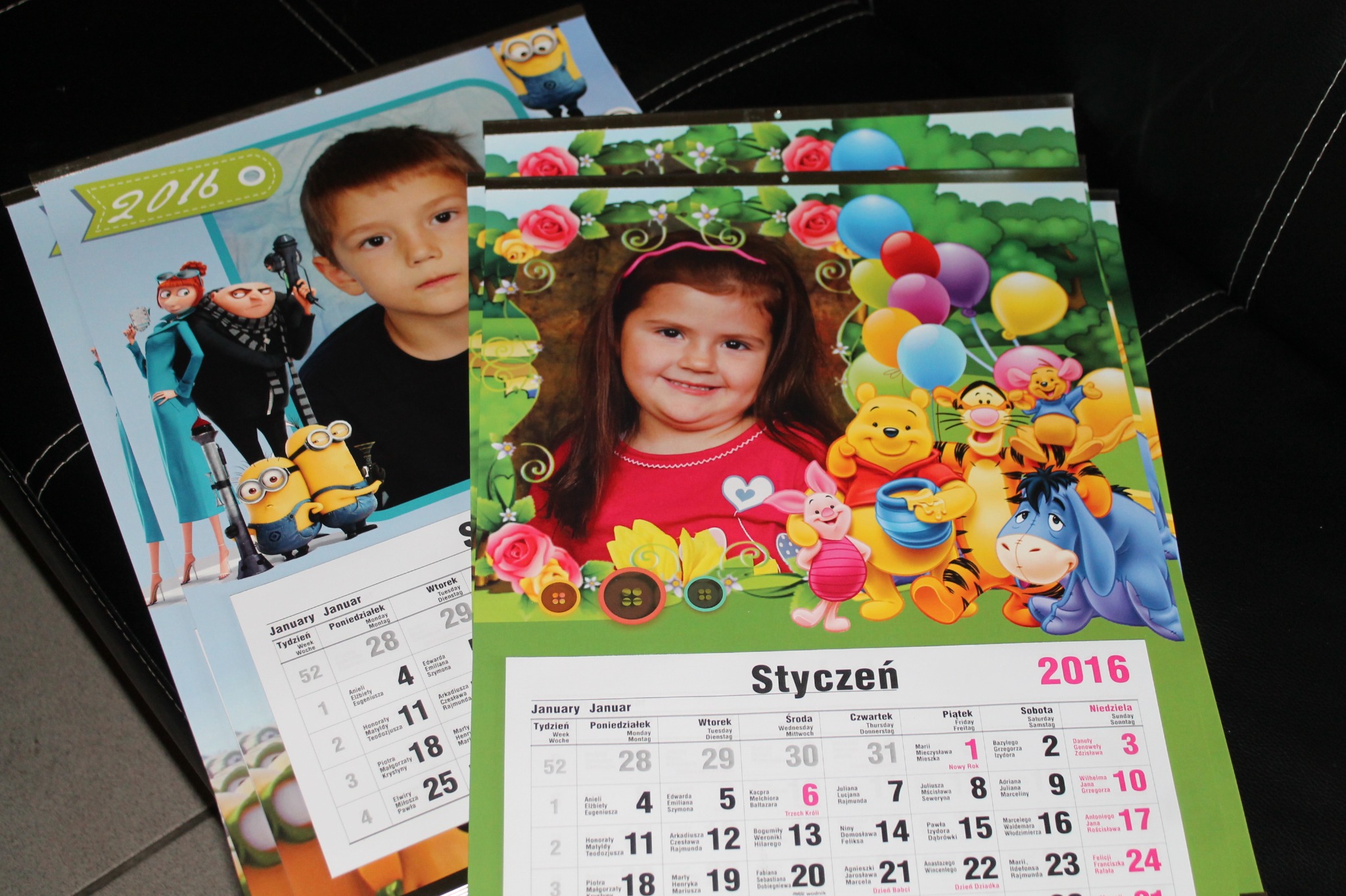 Dwa kalendarze ścienne z nadrukiem zdjęć dzieci, jeden z motywem Minionków i drugi z Kubusiem Puchatkiem, oba otwarte na styczeń 2016.