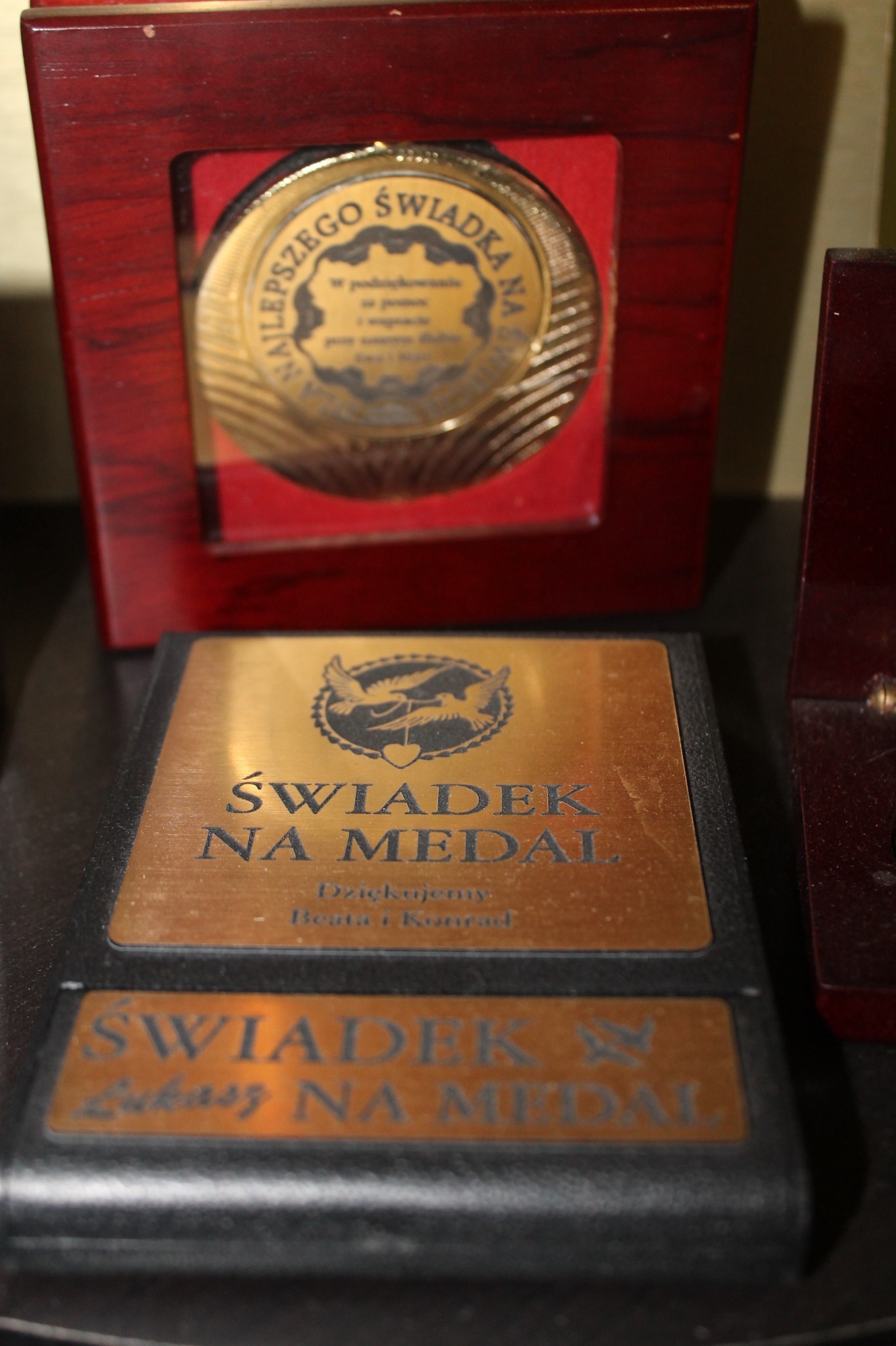 Pamiątkowe medale w drewnianych pudełkach z grawerowanymi tabliczkami, dedykowane dla świadków na medal, z widocznym logo z gołębiami.