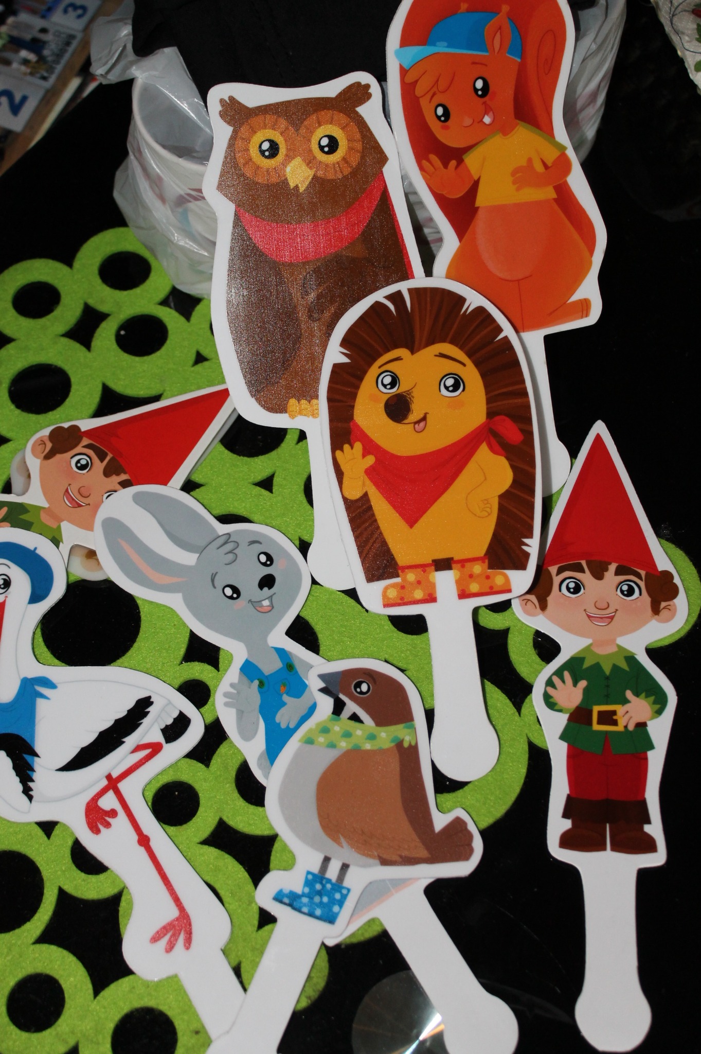 Kolorowe, wycięte naklejki z wizerunkami zwierząt i postaci z bajek, umieszczone na zielonym, wzorzystym tle, gotowe do naklejenia.