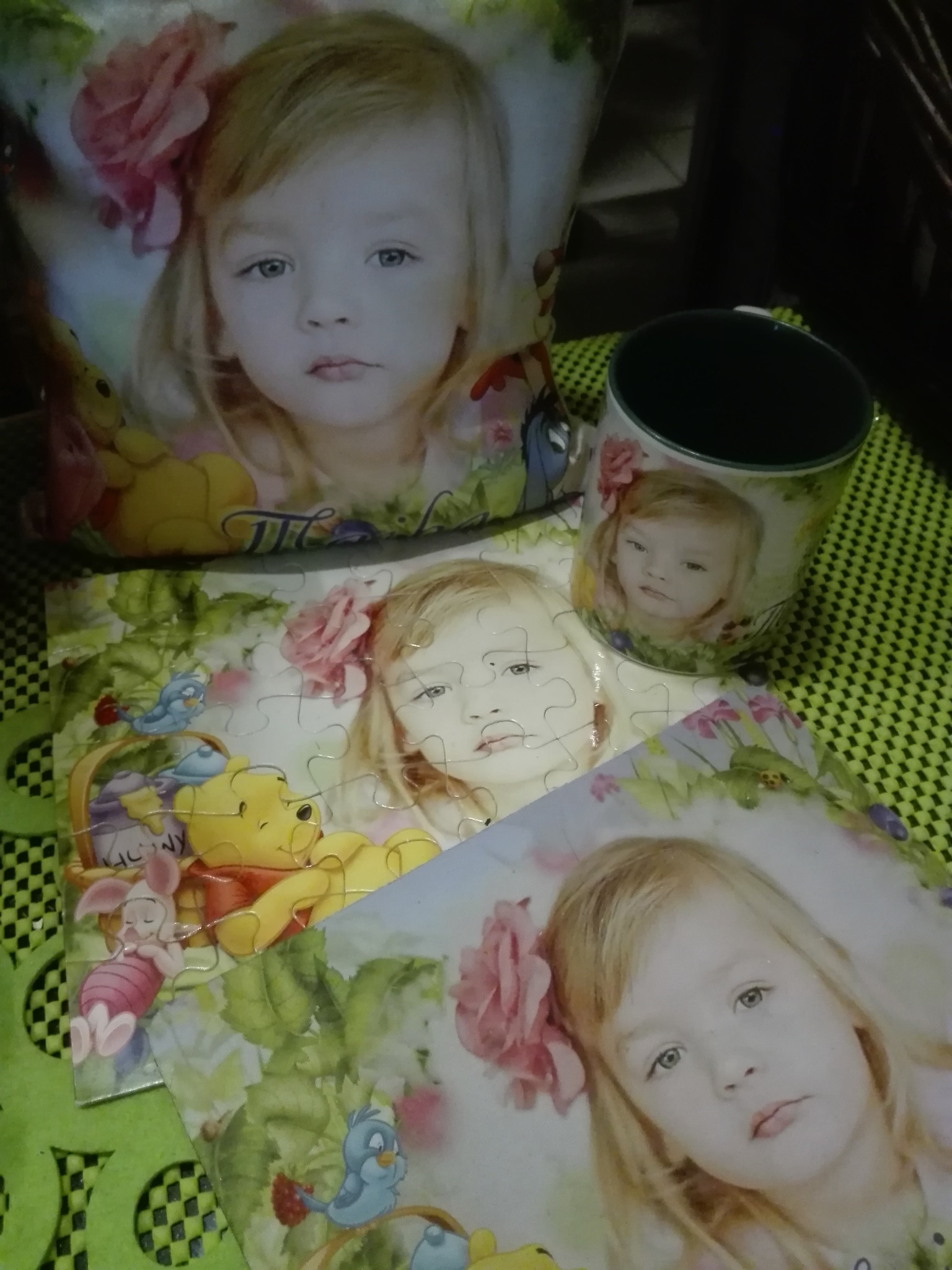 Pamiątki z nadrukiem: poduszka, kubek i puzzle z wizerunkiem dziewczynki z różą we włosach, na tle motywu z Kubusiem Puchatkiem.