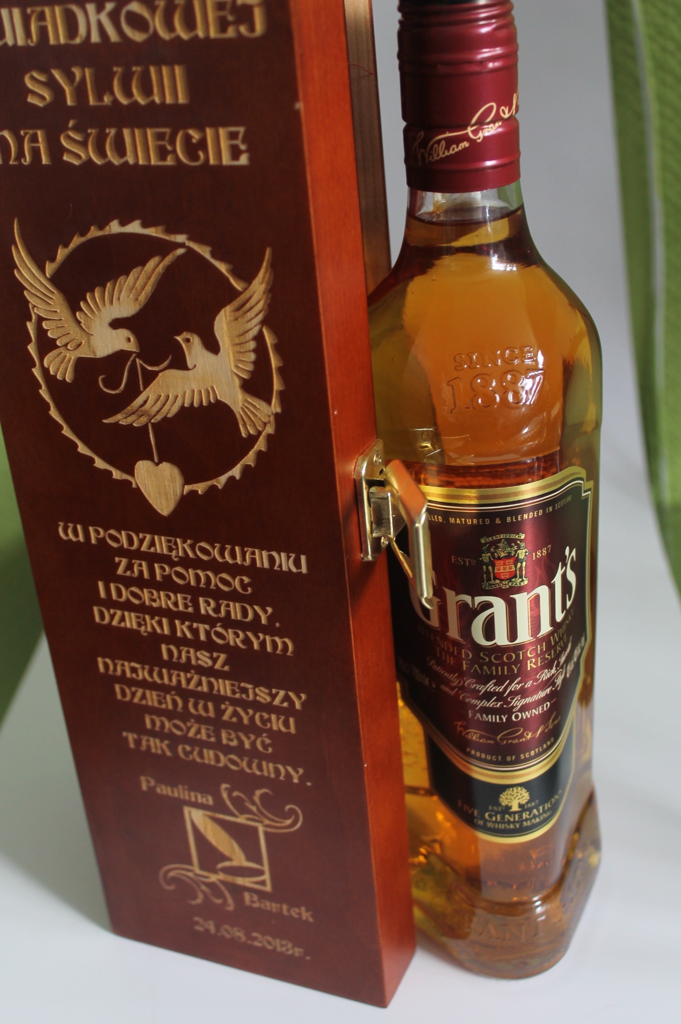 Butelka whisky Grant's obok spersonalizowanej, drewnianej skrzynki z grawerem dedykacji, wykonane w Bydgoszczy.
