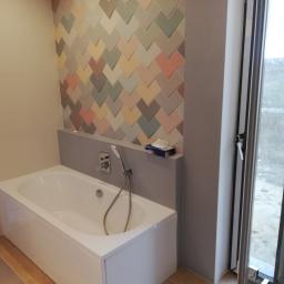 Furman- Bud - Nowoczesna łazienka we Wrocławiu z białą wanną, baterią natryskową i ścianą wyłożoną dekoracyjnymi, wielokolorowymi płytkami w kształcie strzałek, widok na zewnątrz przez okno.