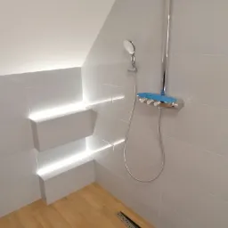 Biała łazienka na poddaszu z nowoczesną armaturą: bateria natryskowa z niebieskimi akcentami i deszczownicą. Ściany wyłożone białymi płytkami z podświetleniem LED w półkach.