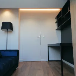 Nowoczesny pokój z ciemnoniebieską sofą, minimalistycznym biurkiem z półkami i ukrytymi drzwiami z oświetleniem LED w suficie.