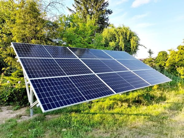Panel słoneczny ustawiony na metalowej konstrukcji na trawiastym terenie z drzewami w tle, widoczne mocowania paneli.
