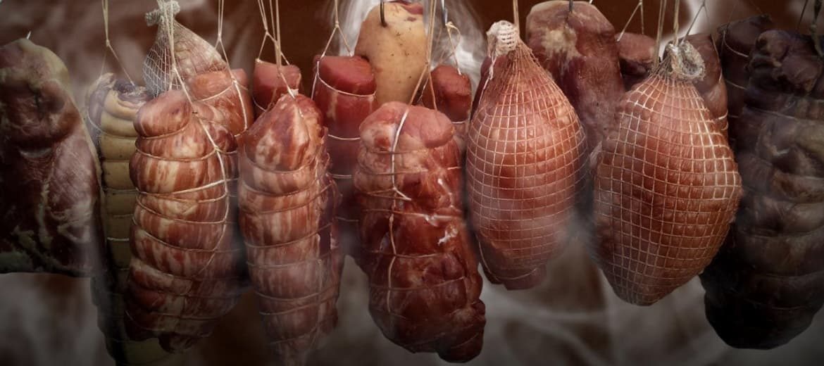 Wędliny i wyroby mięsne wiszące na sznurkach, częściowo w siatkach wędzarniczych, wędzone tradycyjną metodą.