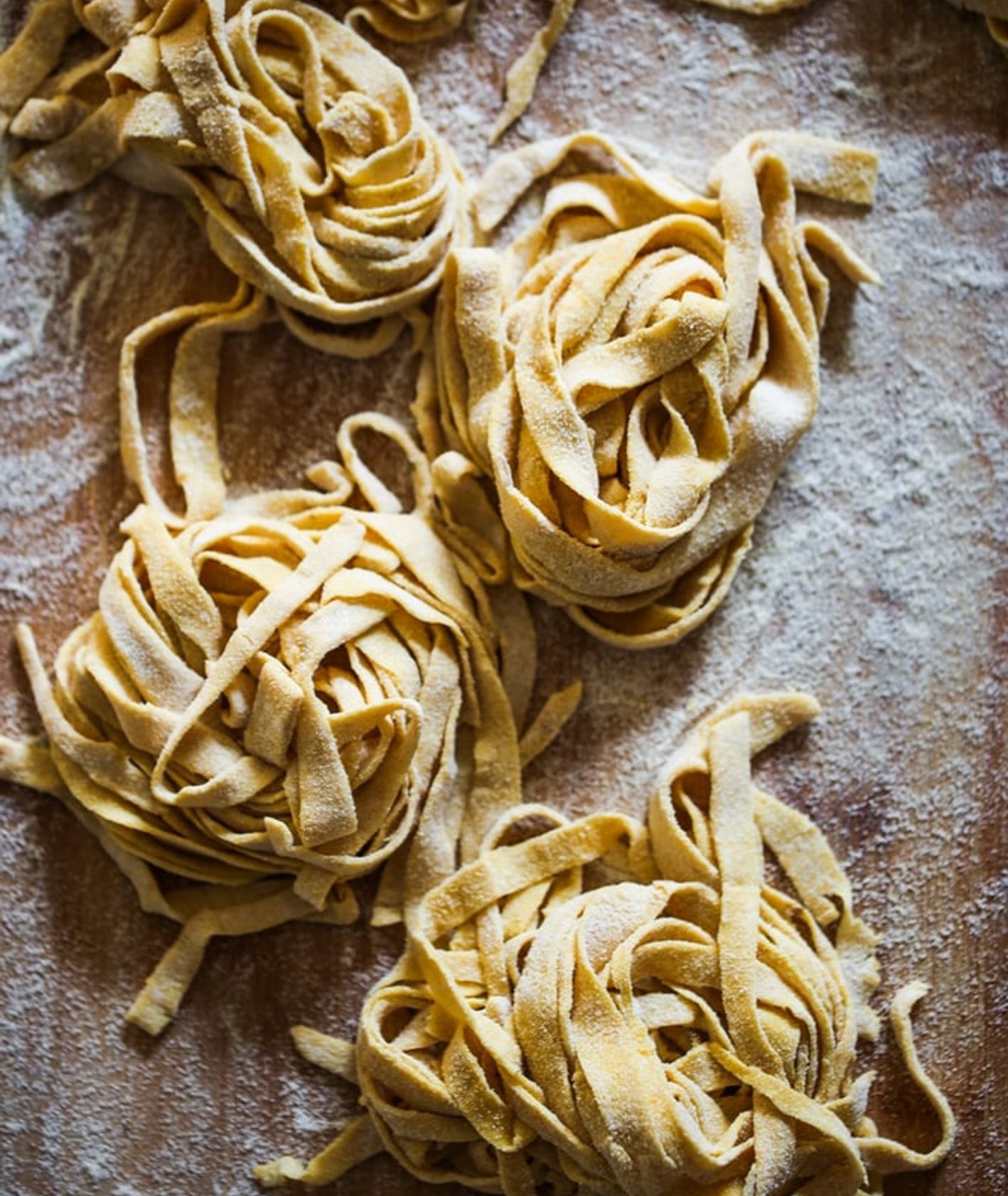 Gniazda świeżego makaronu tagliatelle posypane mąką na drewnianym blacie, przygotowane do gotowania.