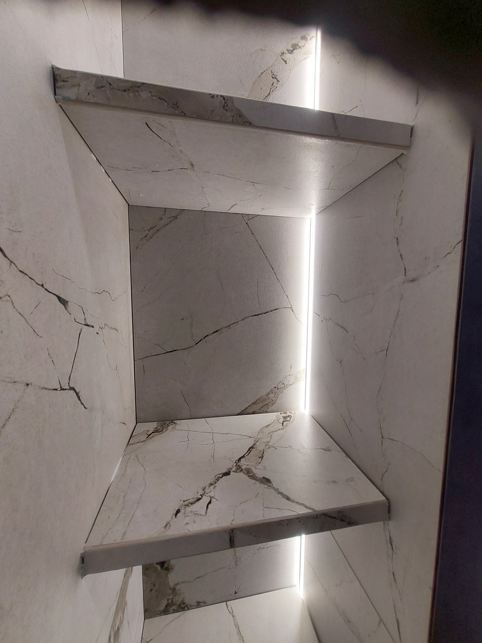 Półki z płytek imitujących marmur z podświetleniem LED wnęki, widok z dołu.