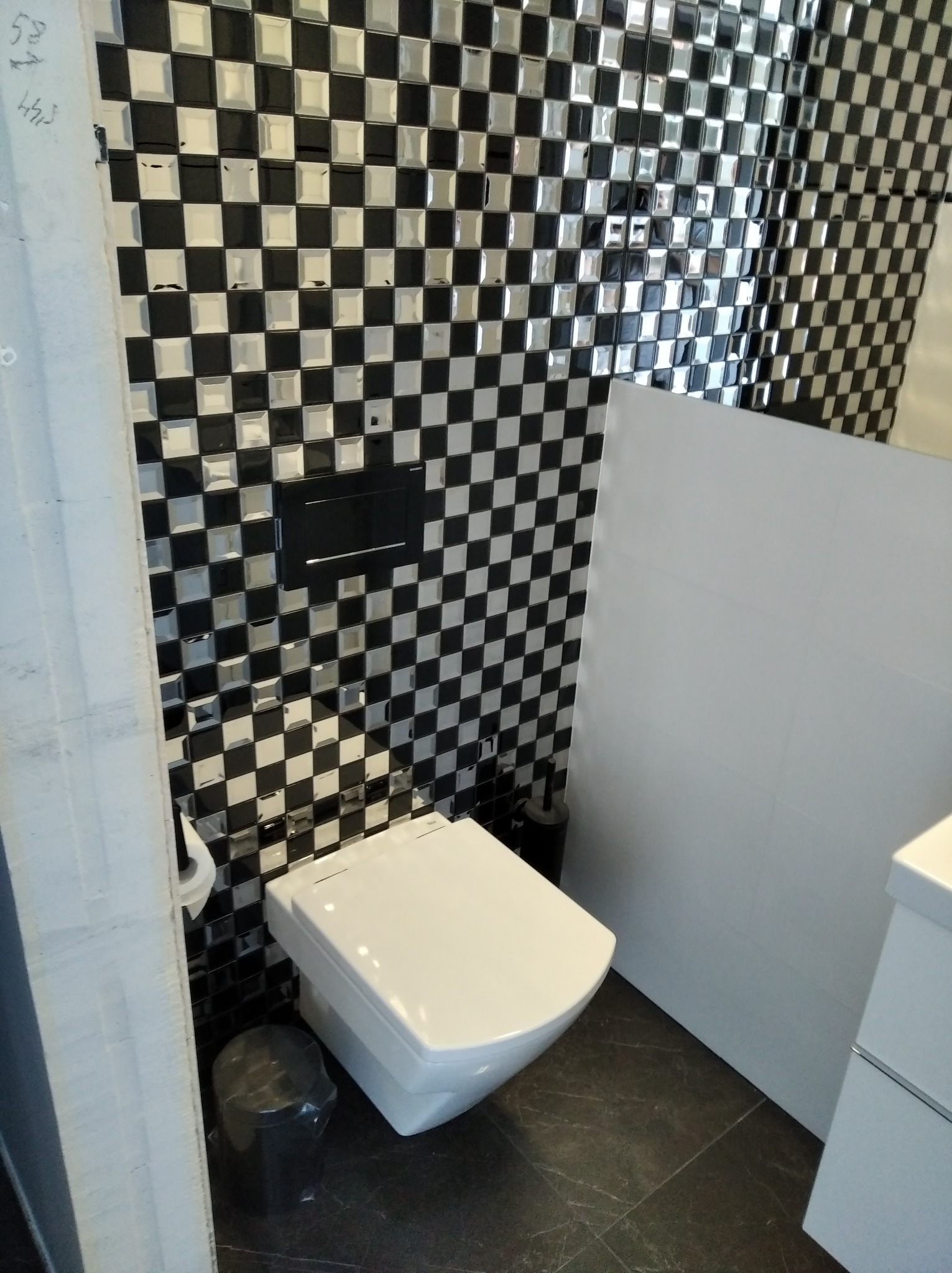 Nowoczesna toaleta wisząca z czarno-białą szachownicą na ścianach, podwieszany system spłukiwania i ciemna podłoga.