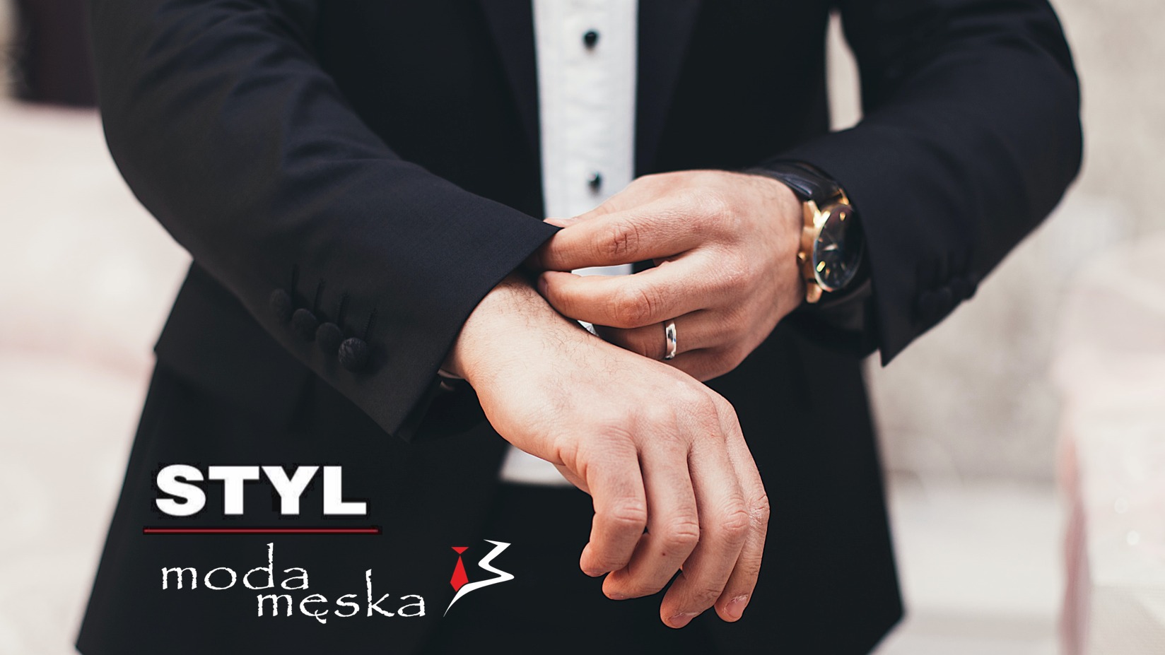 Mężczyzna w czarnym garniturze zapinający mankiet koszuli, widoczny zegarek z czarnym paskiem i złotą tarczą oraz srebrny pierścionek.