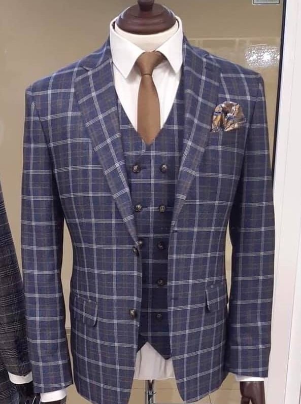 Elegancki, trzyczęściowy garnitur męski w niebiesko-szarą kratę, z brązowym krawatem i poszetką w brązowo-złote wzory, prezentowany na manekinie.