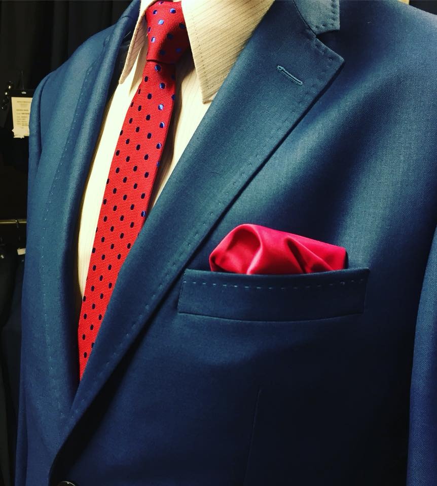 Granatowy męski garnitur z czerwoną poszetką i krawatem w niebieskie kropki, prezentowany na manekinie.