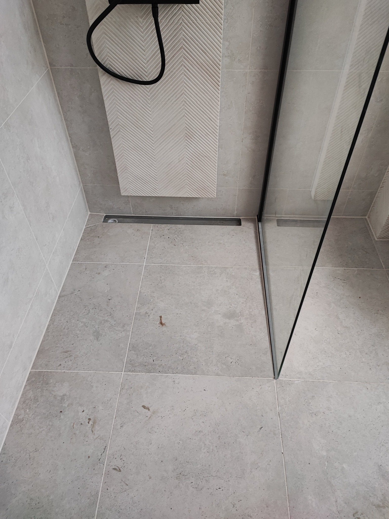 Szare płytki w kabinie prysznicowej z odpływem liniowym i grzejnikiem drabinkowym z dekoracyjnym wzorem w jodełkę. Minimalistyczny design.