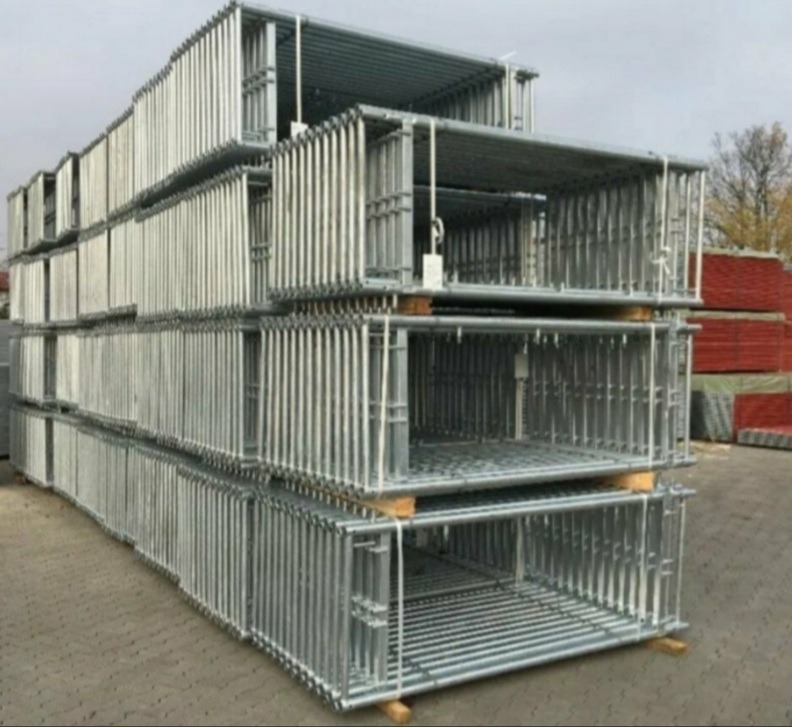 Stalowe ramy rusztowań modułowych ułożone w stosy na drewnianych paletach, przygotowane do transportu lub magazynowania, widoczne elementy konstrukcyjne i zabezpieczenia.