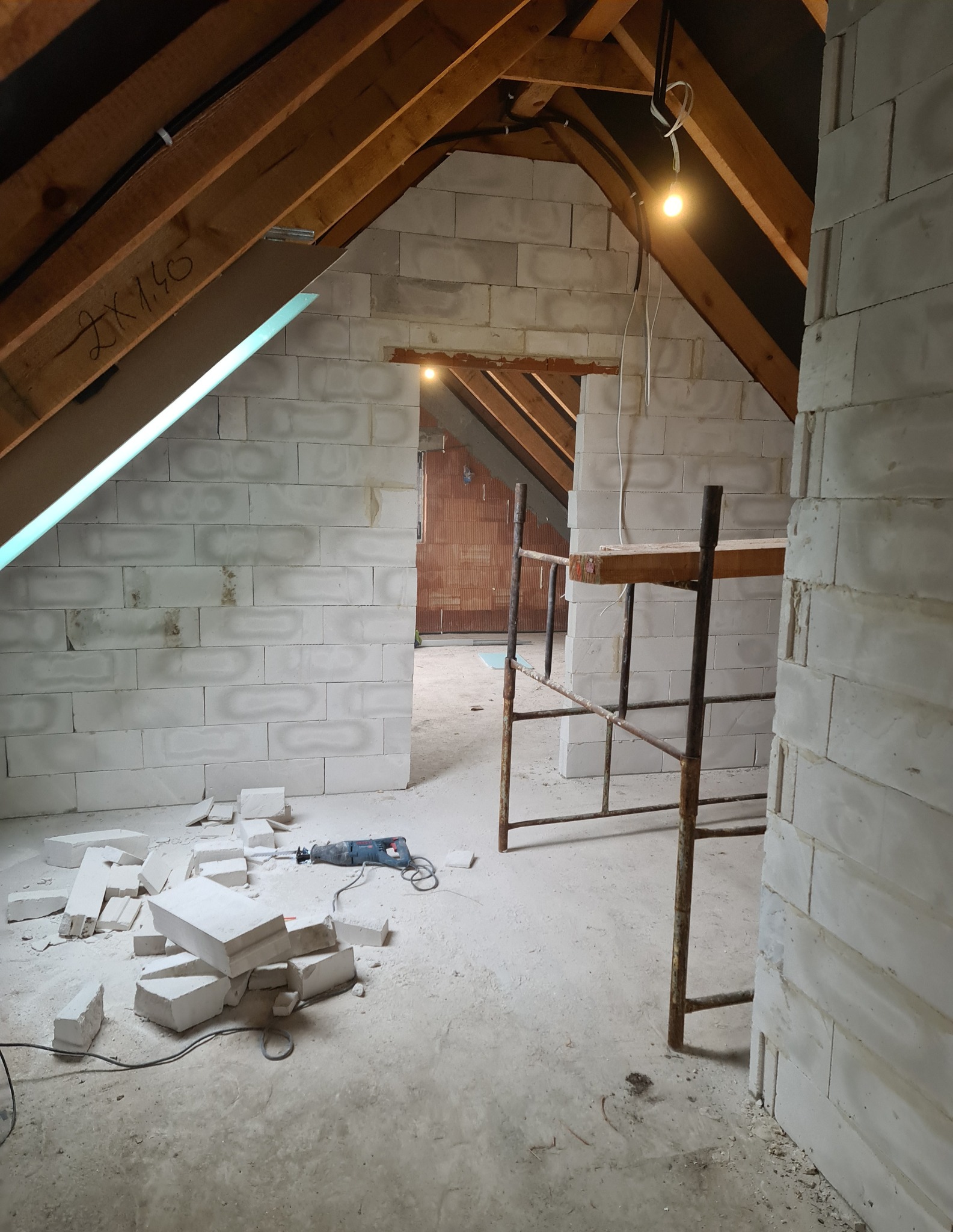 Wnętrze poddasza w trakcie budowy ścian działowych z betonu komórkowego, widoczne rusztowanie i narzędzia, drewniana konstrukcja dachu.