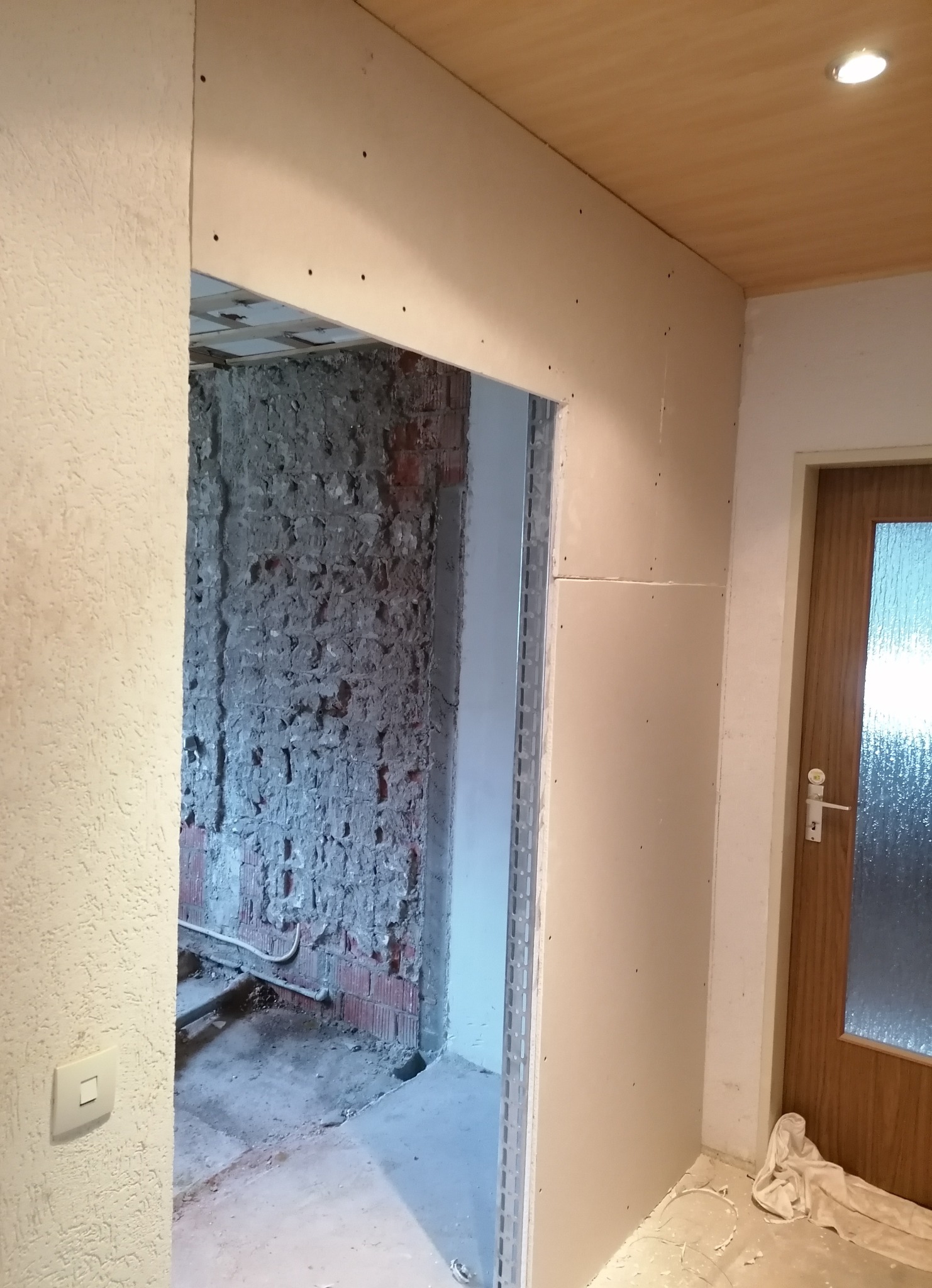 Montaż ościeżnicy z płyt gipsowo-kartonowych przy wejściu do remontowanego pomieszczenia z odsłoniętą cegłą i instalacjami.