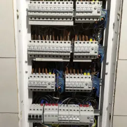 Rozdzielnica elektryczna z zainstalowanymi bezpiecznikami EATON i GEYA, widok z bliska na okablowanie i elementy zabezpieczające w skrzynce na ścianie wyłożonej płytkami.