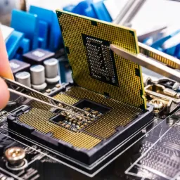 Instalacja procesora w gnieździe płyty głównej za pomocą precyzyjnych szczypiec, widoczne elementy płyty głównej i radiator