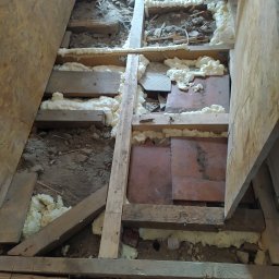 Remonty wykończenia wnętrz - Podłoga w trakcie remontu: widoczne drewniane legary, izolacja pianką montażową, fragmenty starej posadzki i płyty OSB, buty robocze w tle.