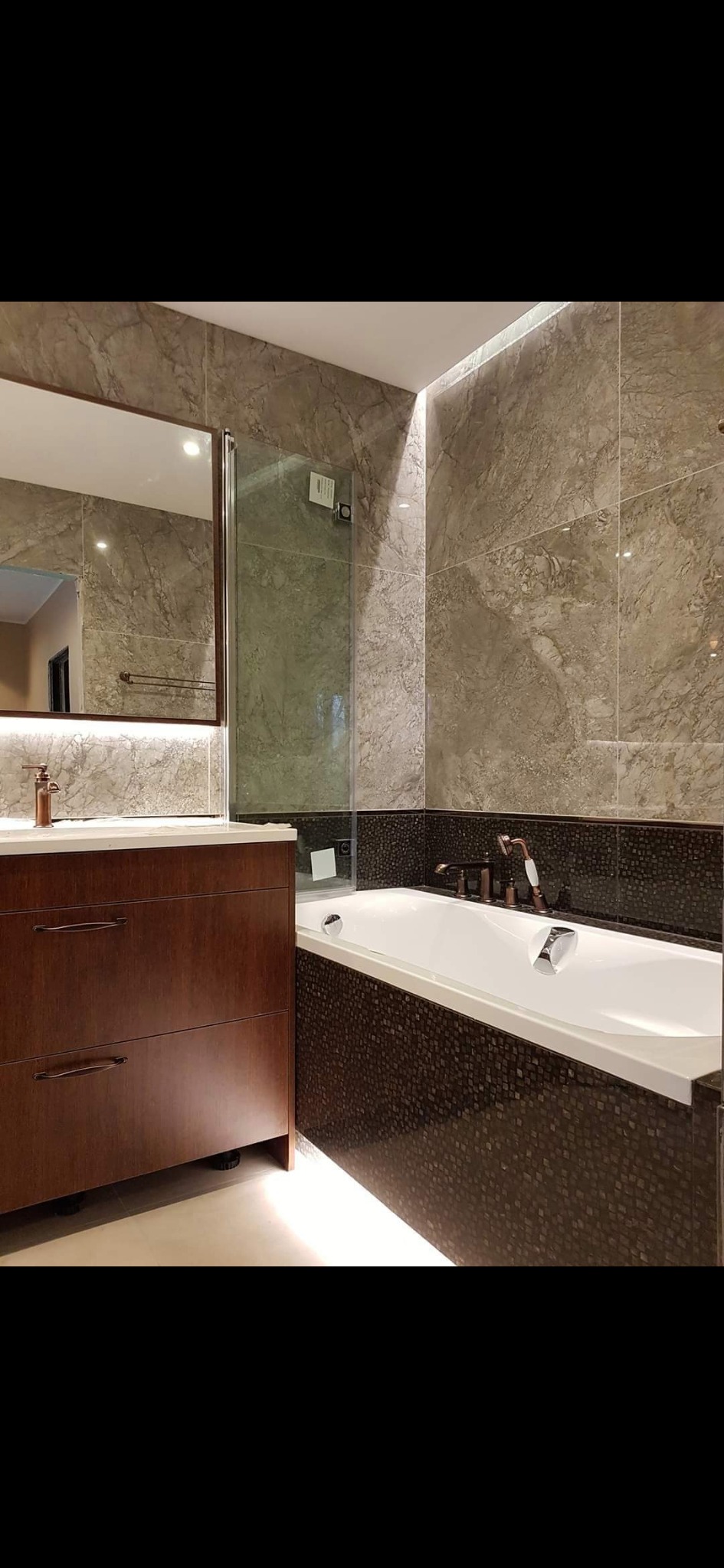 Nowoczesna łazienka z marmurowymi płytkami, drewnianą szafką pod umywalką i wanną obudowaną mozaiką.