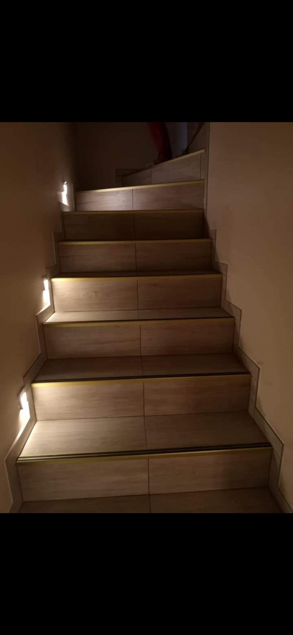 Wykończone schody wewnętrzne wyłożone płytkami imitującymi drewno z subtelnym oświetleniem LED w ścianie.