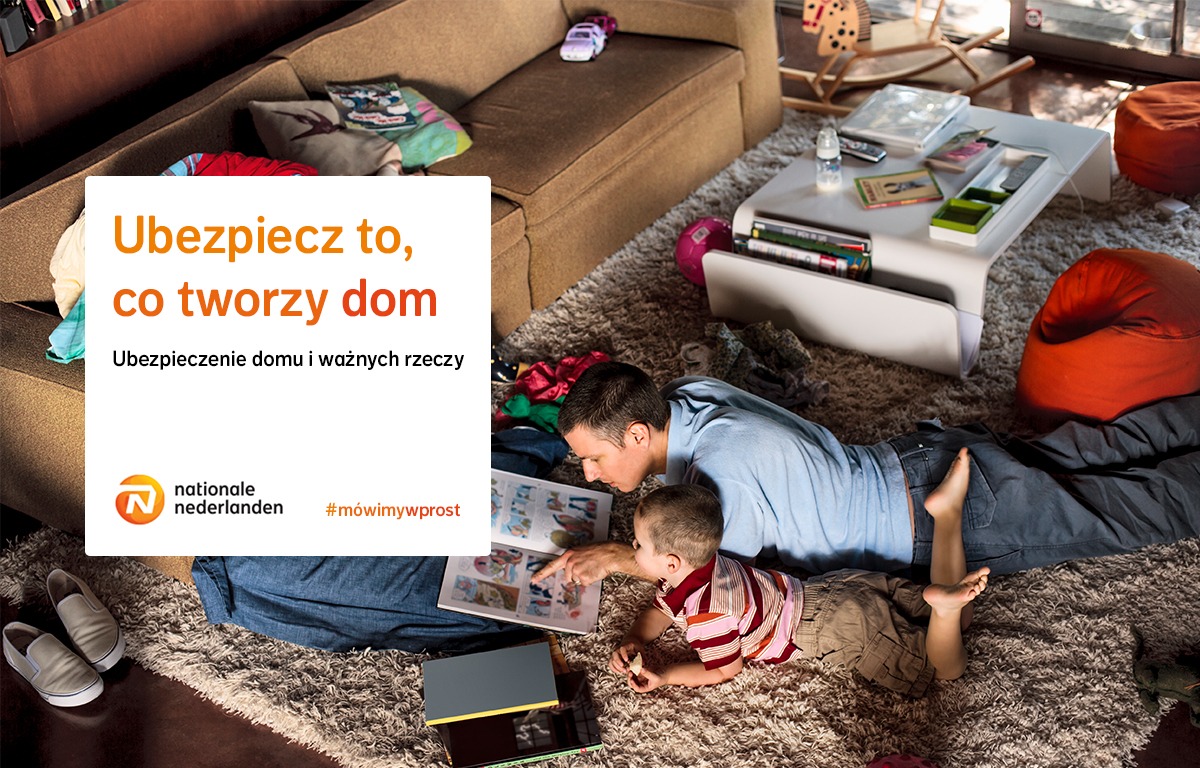 Ojciec z synem leżą na dywanie w salonie, oglądając książkę z obrazkami; w tle sofa, stolik kawowy z zabawkami i pufy; widoczny fragment reklamy towarzystwa ubezpieczeniowego z hasłem 'Ubezpiecz to...