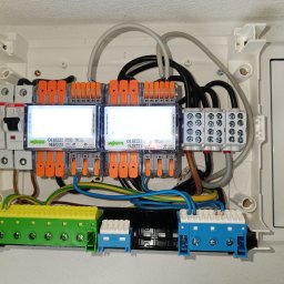 Tania firma z Ukrainy posiadająca Niemieckie doświadczenie - Otwarta skrzynka elektryczna z zainstalowanymi bezpiecznikami, złączkami WAGO i przewodami w różnych kolorach. Widoczne elementy instalacji wewnątrz białej obudowy.