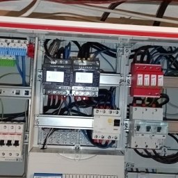 Tania firma z Ukrainy posiadająca Niemieckie doświadczenie - Otwarta szafa rozdzielcza z kompletnym okablowaniem, zabezpieczeniami i modułami pomiarowymi. Widoczne elementy instalacji elektrycznej wewnątrz obudowy.