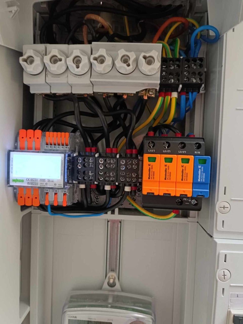 Szczegółowe ujęcie wnętrza skrzynki elektrycznej z bezpiecznikami, modułami Wago, warystorami Weidmüller i licznikiem energii elektrycznej.